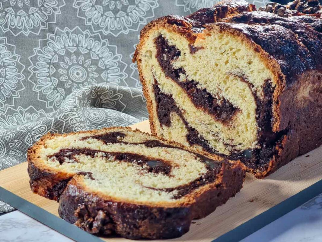 The cozonac sat on a wooden board, with a slice cut open, flat on the board. You can see the cocoa and walnuts filling inside, which looks like a swirl through the sweet bread