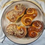 A silver plate with a golden rim, with four mucenici on it. Two of them are glazed with honey, whilst the other two are glazed and covered with chopped walnuts