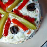 A close-up of the Beouf Salad on a round platter. It is decorated with slices of pickles, pickled red pepper and olives