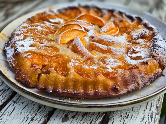 A close-up of the apricot tart, sitting on a grey plate. It is photographed outside, on a white wooden table.