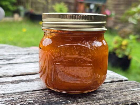 A jar filled with apricot jam, on a white wooden table, outdoors.