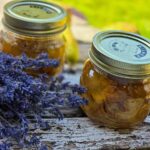 Romanian Pear And Lavender Jam Recipe – Gem de Pere cu Lavanda Two jars with the dark yellow jam inside, on a wooden table, next to a bunch of lavender.