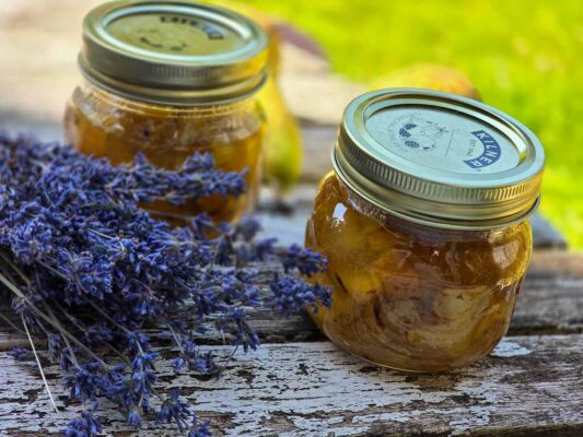 Two jars with the dark yellow jam inside, on a wooden table, next to a bunch of lavender.