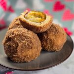 Romanian Plum Dumplings Recipe – Galuste Cu Prune Three dumplings on a grey plate, with a dumpling cut in half to see the plum inside, on top.