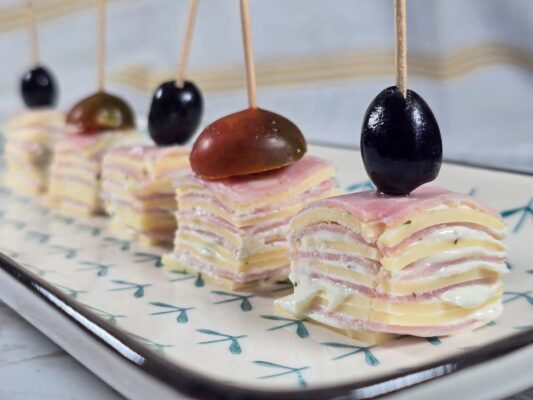 Stacks of ham and cheese, with cream cheese in between. Some are topped with black olives, some with cherry tomatoes cut in half.