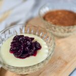Romanian Semolina Pudding Recipe – Gris Cu Lapte A close-up of a glass bowl filled with the white semolina pudding, topped with sour cherry jam
