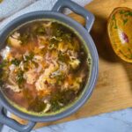 Romanian Red Orach Soup Recipe – Ciorba de Loboda The soup, which has a pink hue, inside a grey container, on a wooden board.