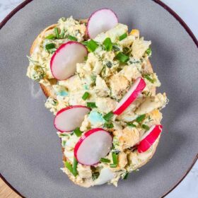 A slice of bread topped with the egg salad, which is topped with slices of red radishes