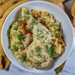 Romanian Chicken Pilaf Recipe – Pilaf cu Pui A deep white plate with the yellow pilaf in it, topped with a chicken leg and plenty of chopped dill. Around the bowl there is a yellow tea towel.
