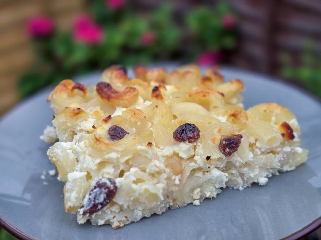 A close-up of a slice of the macaroni pudding on a grey plate
