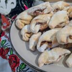 A plate with the walnut and plum jam cookies on top of each other, next to a Christmas tree