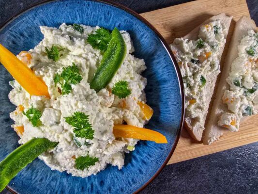 The cream cheese and peppers dip in a blue bowl, decorated with slices of green and yellow pepper, and parsley