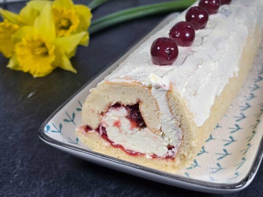 The finished roulade, with cherries on top, next to a bunch of yellow daffodils