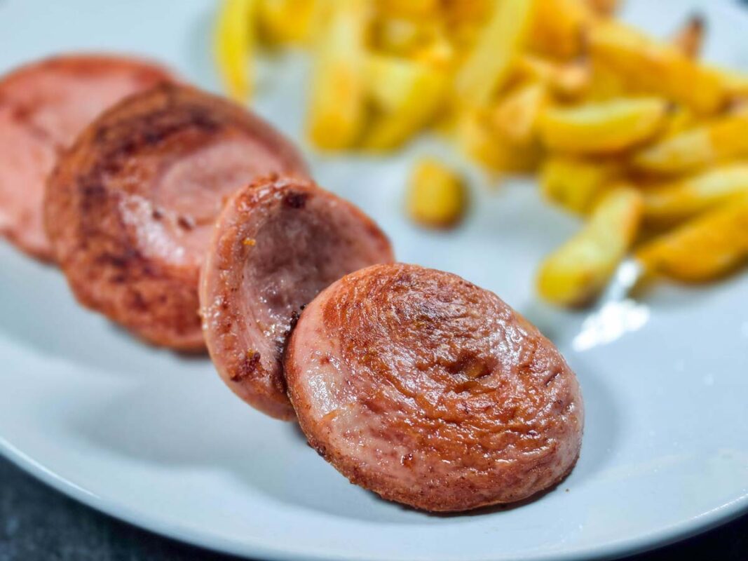 A close-up of four slices of fried parizer alongside fries, on a white plate.