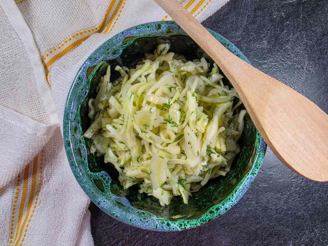 The cabbage salad inside a green and blue bowl, with a wooden spoon on the edge